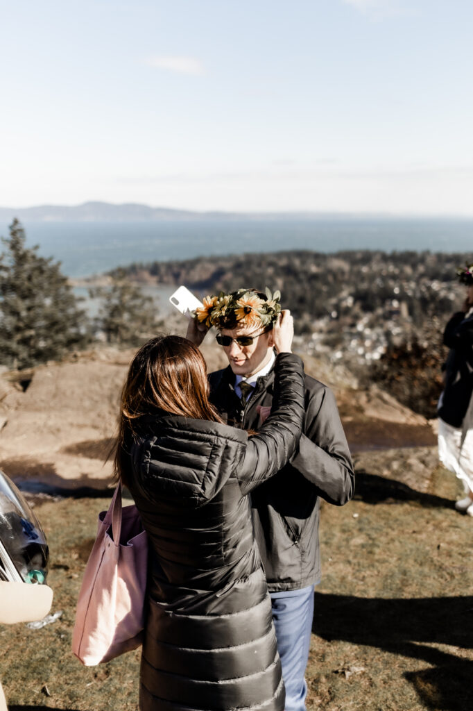 A friend helps place a flower crown on the grooms head at a Mount Douglas Elopement.