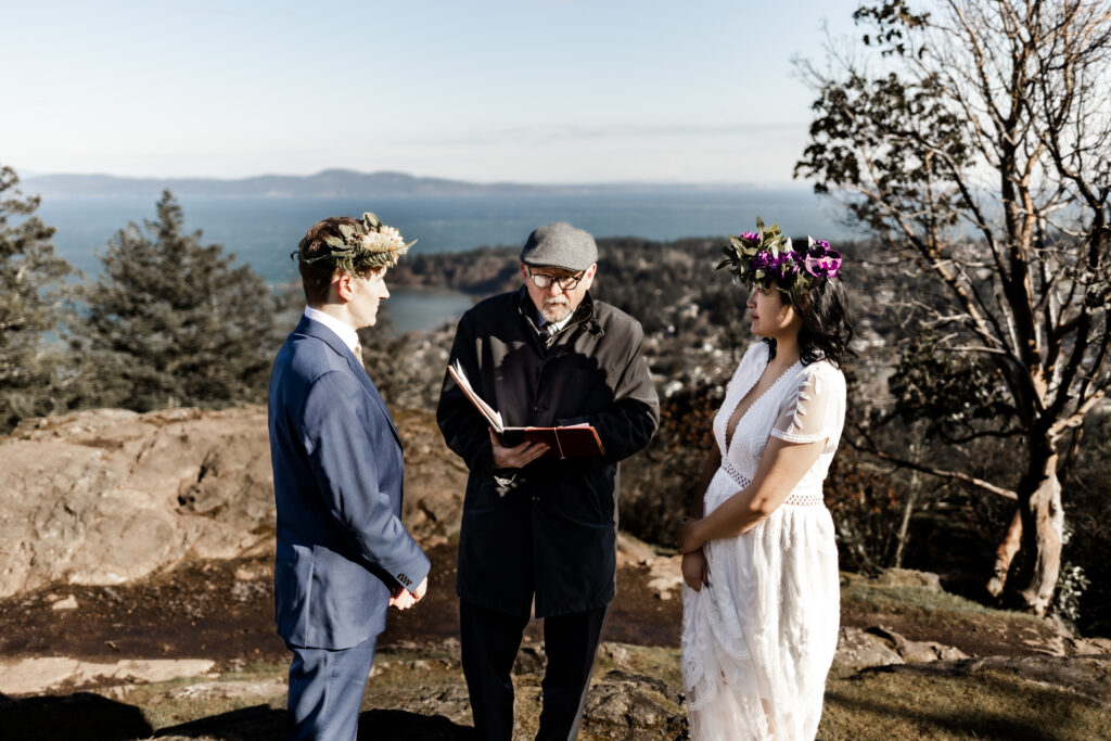 A couple stands in front of the officiant with an ocean background at a Mount Douglas elopement.