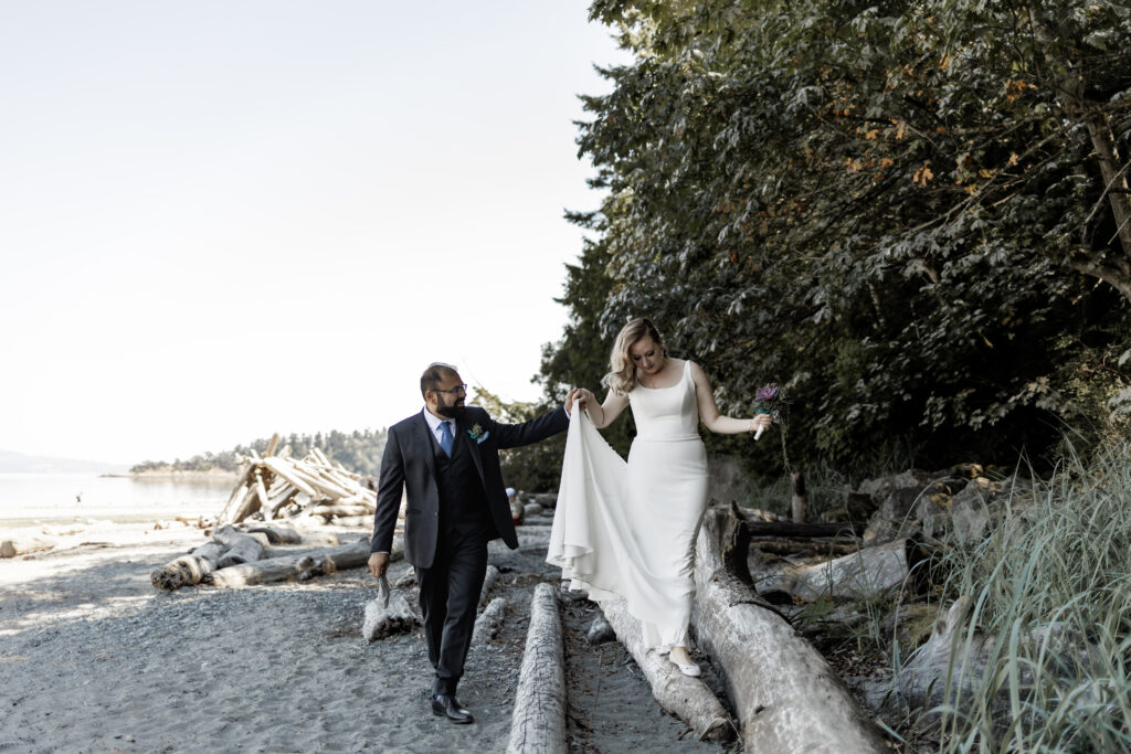 Bride and groom walking on logs at Mount doug beach at this Victoria wedding