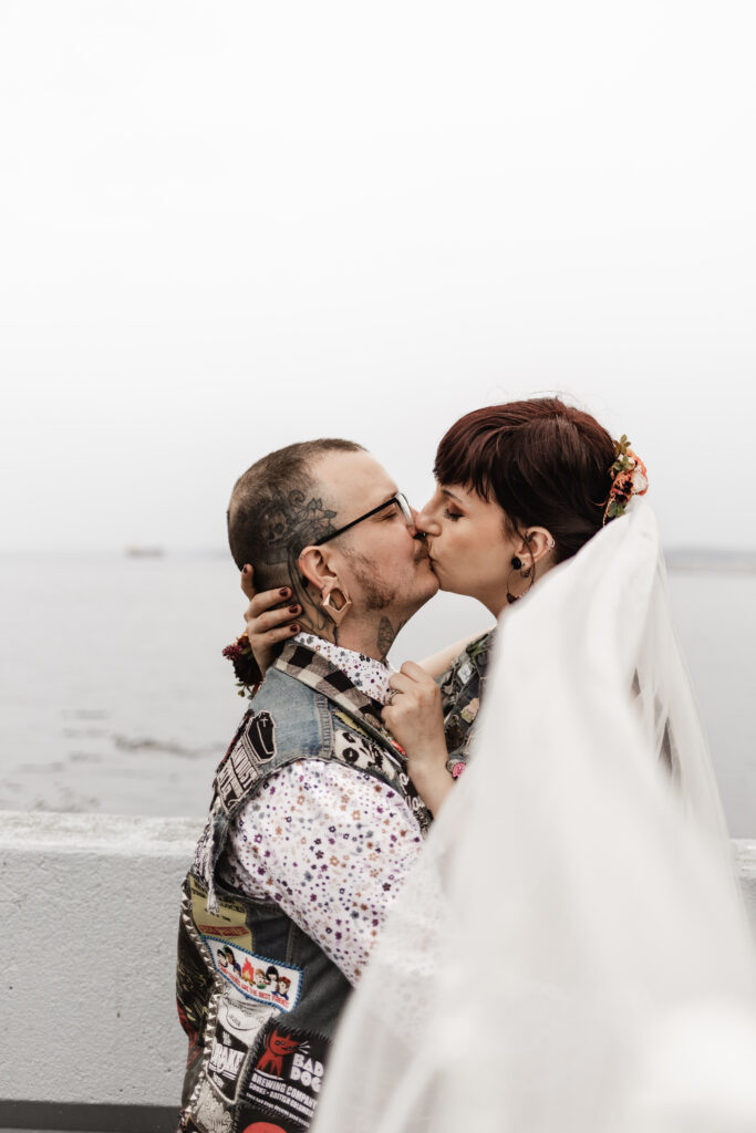 bride and groom share a kiss at saxe point park in front of an ocean view at this punk wedding in Victoria, BC