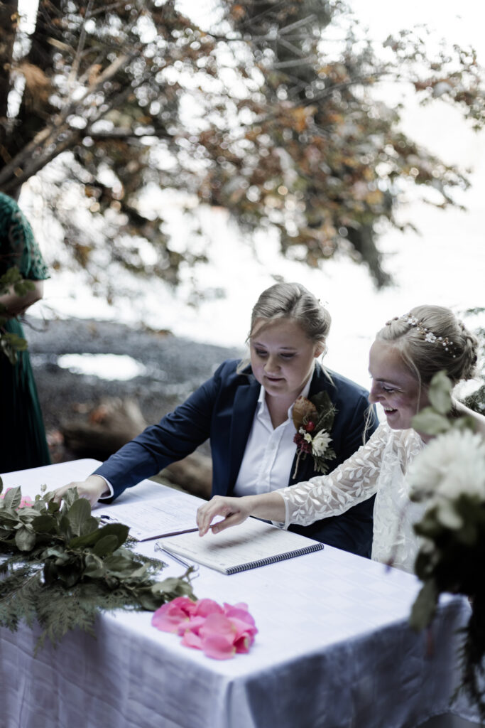 The couple signs their marriage papers together at this Camp Elphinstone wedding.