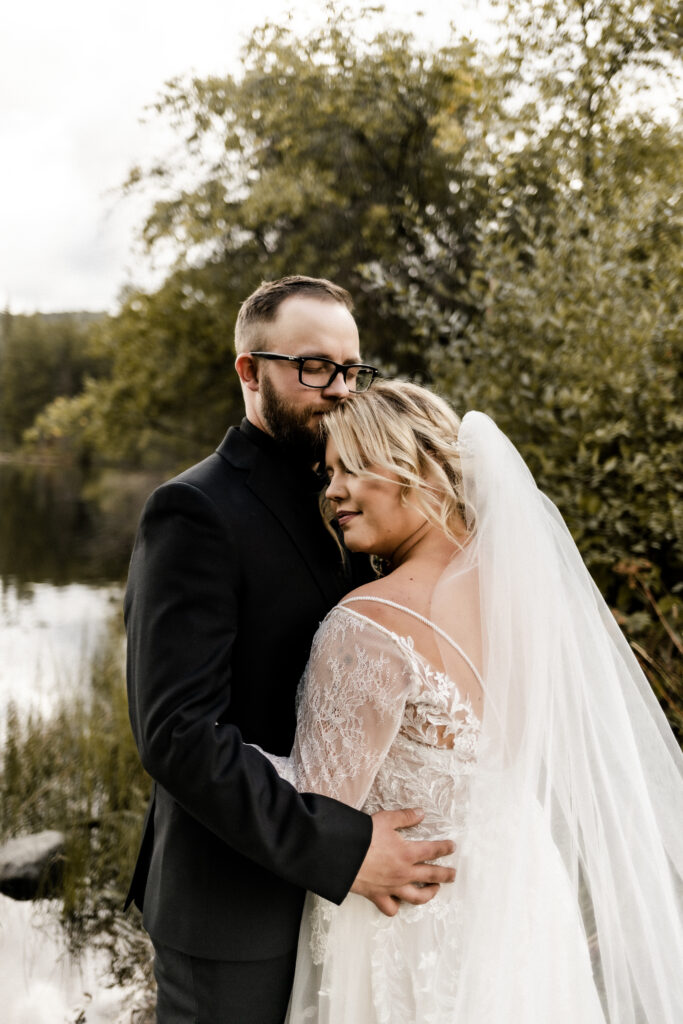 The couple embrace in front of a lake at this cabin elopement