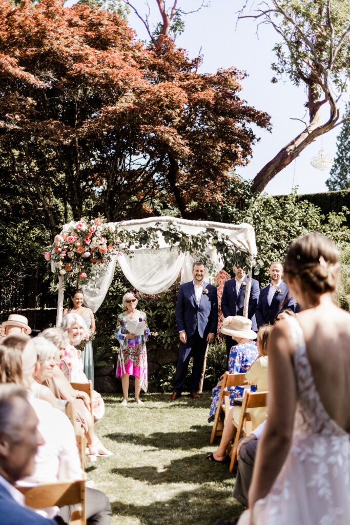 The groom smiles as the bride walks down the aisle at this garden party wedding.