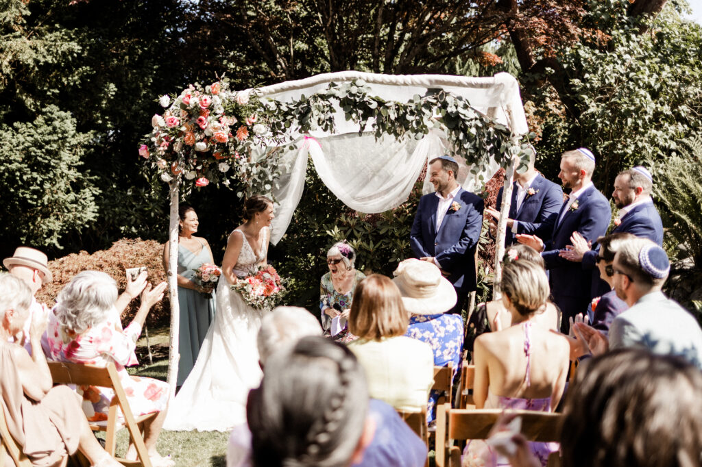 The bride and groom stand together under the chuppah at their garden party wedding.