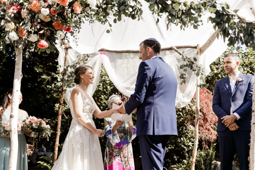 The bride and groom exchange rings under the chuppah at their garden party wedding.