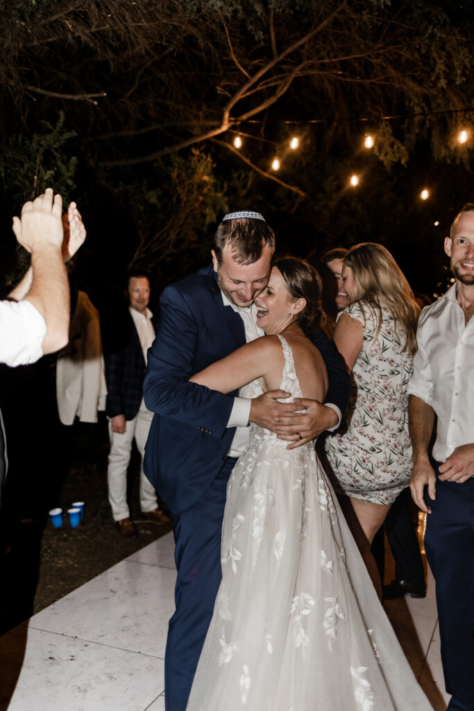 The couple hug on the dance floor surrounded by friends at their garden party wedding