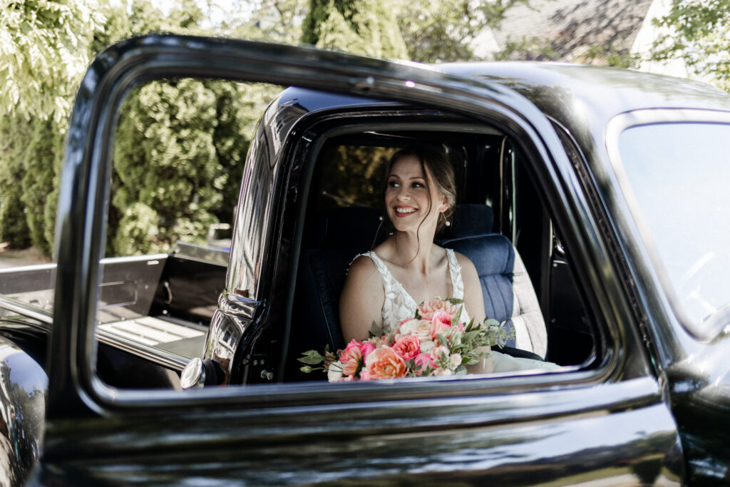 The bride poses in a vintage black truck with her flowers at this garden party wedding