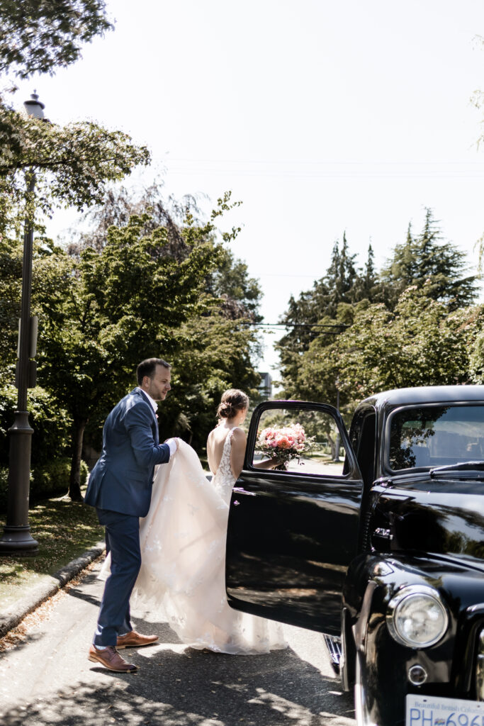 The groom helps the bride climb in the vintage black truck at their garden party wedding