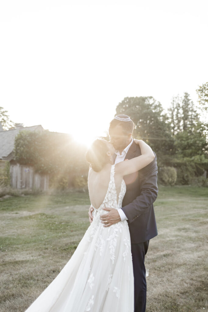 The bride and groom share a kiss as the golden hour sun shines in from behind at their garden party wedding