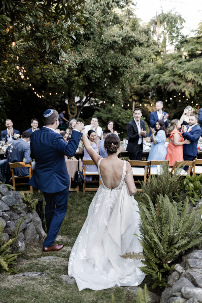 The bride and groom enter their reception holding hands high in the sky at their garden party reception