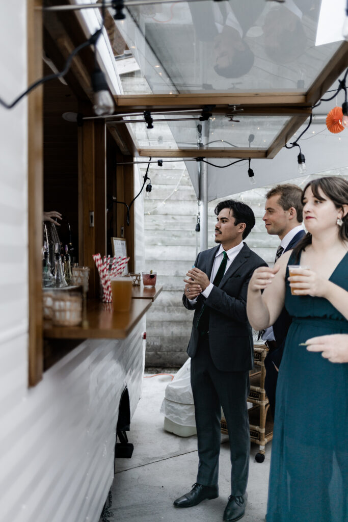 Guests wait to order at the bar at this Camp Elphinstone wedding.