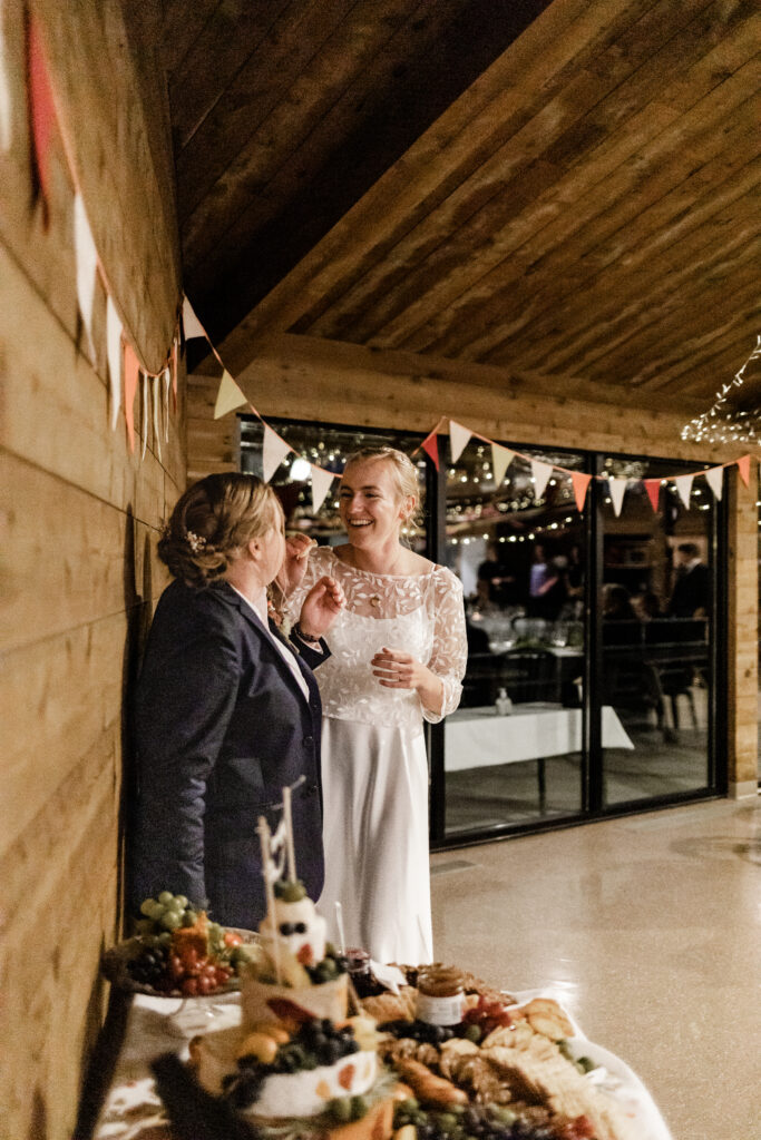 The couple feed each other a piece of cheese from their characuterie table at this Camp Elphinstone wedding.