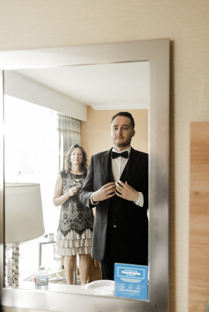 Groom adjusts his suit in the mirror as his mother watches at this downtown Vancouver wedding