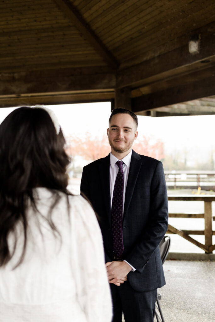 Groom smiles at bride at their ceremony at Rocky Point Park