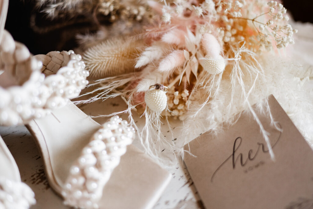 Up close of the wedding details including the bride's shoes, ring, bouquet, and vow books at this Kildara Farms Wedding