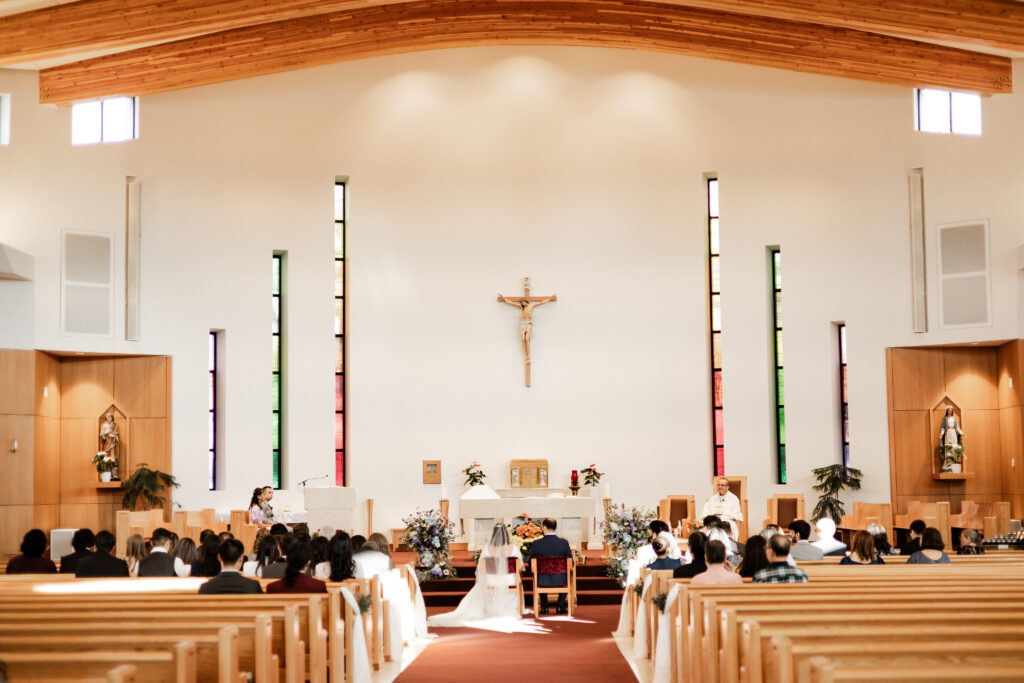 Bride and groom sit together at the end of aisle of St. Paul's Parish at their wedding at Seasons Restaurant