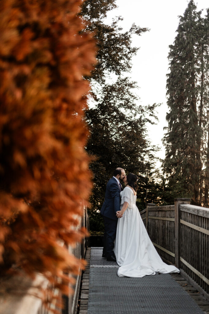 Bride and groom share a kiss on the wood bridge at Queen Elizabeth Park at this wedding at Seasons Restaurant