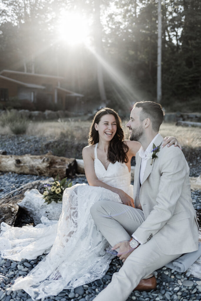 The couple sit beside each other on a log with the sun shining through the trees behind them at their east sooke elopement.