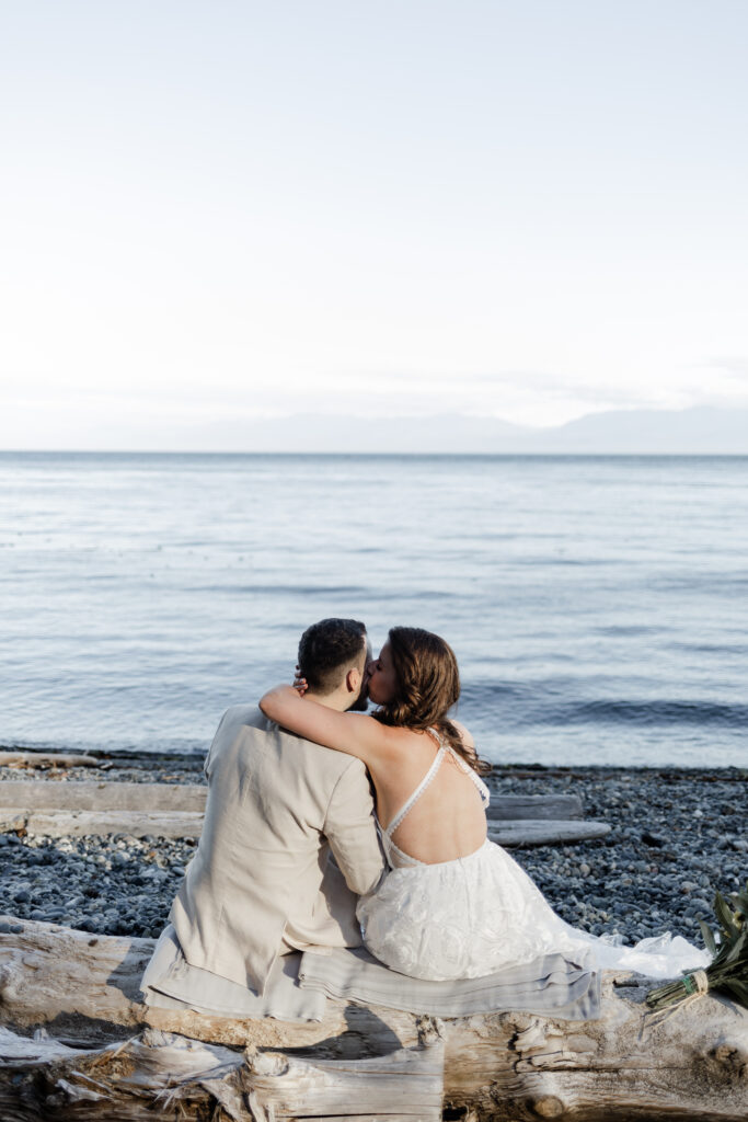 The bride gives the groom a kiss on his cheek as he admires the blue ocean view at their east sooke elopement.