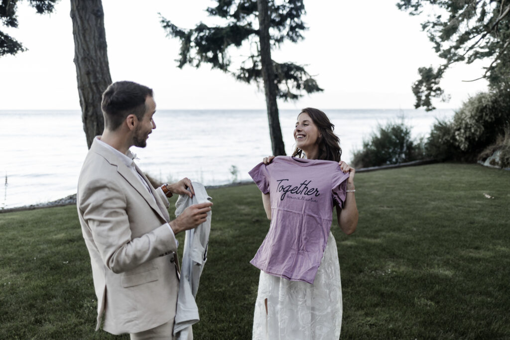 The married couple hold up their gifts to show each other, which are custom made t-shirts, at their east sooke elopement.