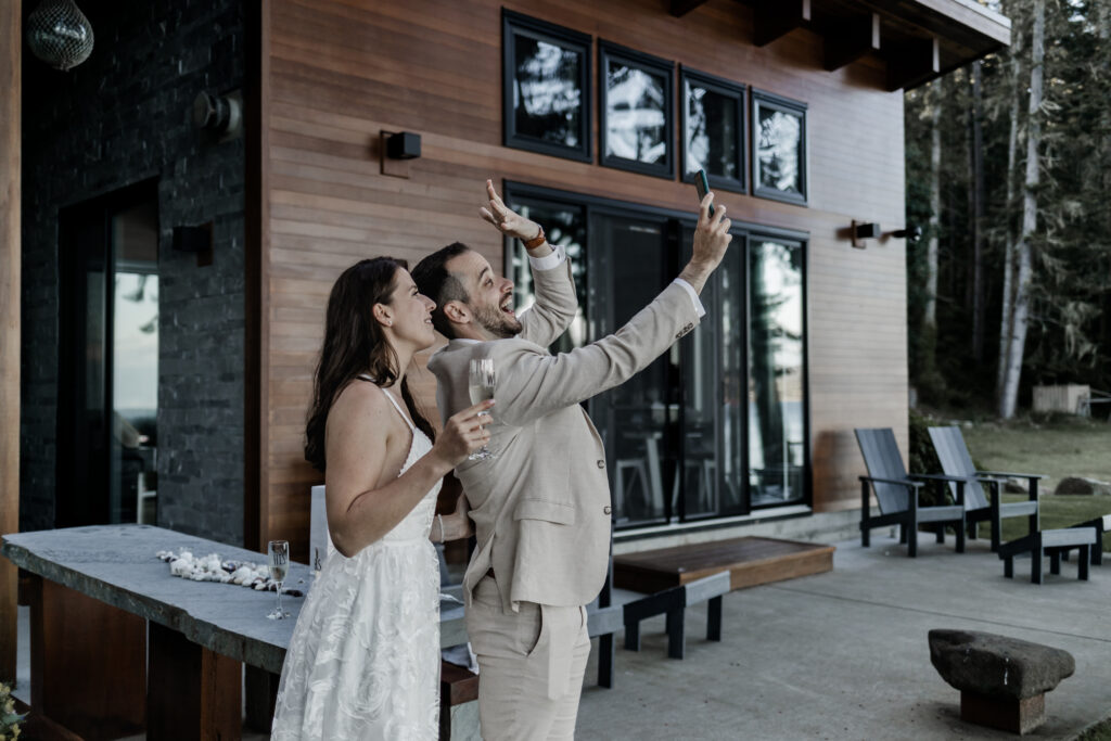 The bride and groom take a selfie together, holding up their hands to show off their wedding rings.