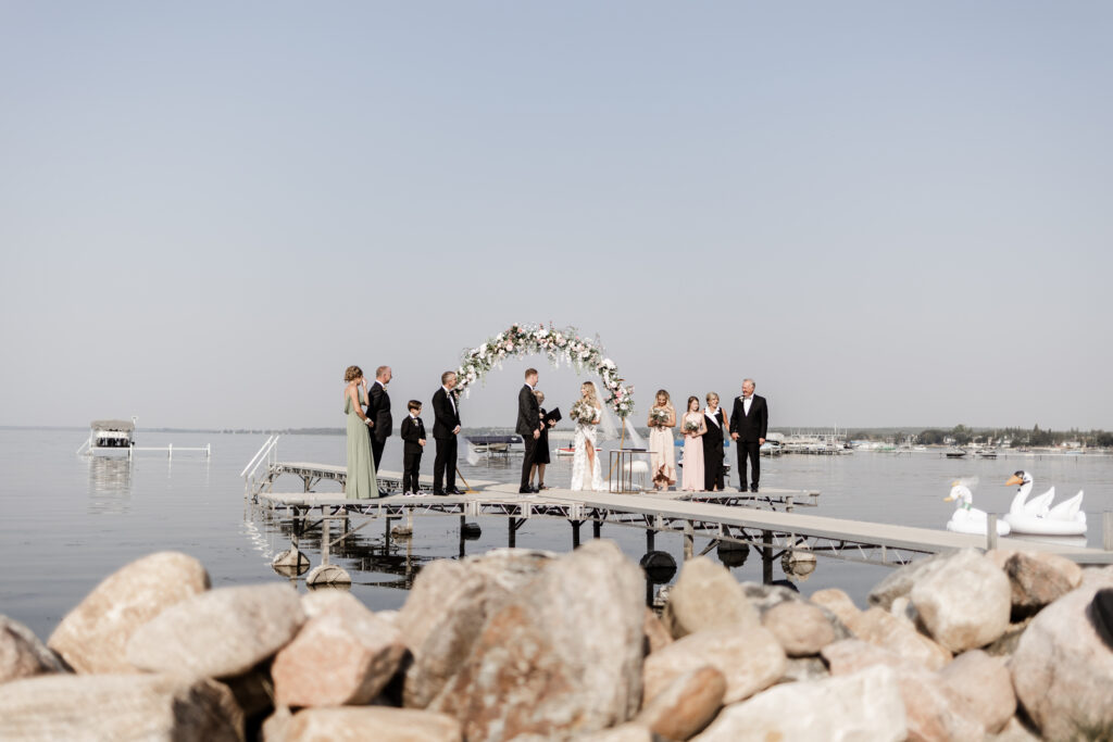 The couple and their bridal party stand on a dock for the ceremony at this lakeside wedding at Alberta Beach