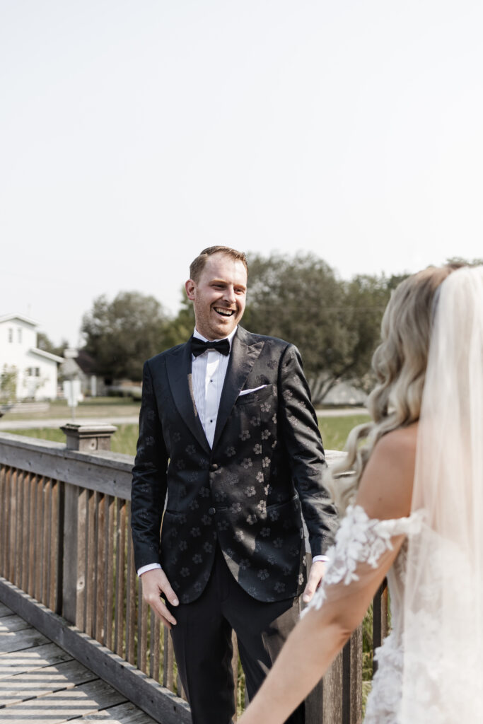 The groom smiles in delight seeing his bride during their first look at this lakeside wedding at Alberta Beach