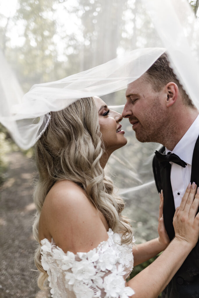 bride and groom touch noses underneath the veil at this lakeside wedding at Alberta Beach