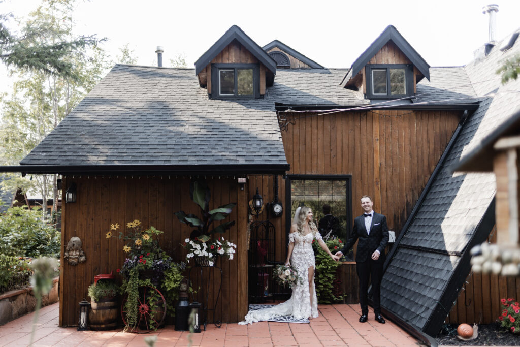 bride and groom pose in front of a cabin at this lakeside wedding at Alberta Beach