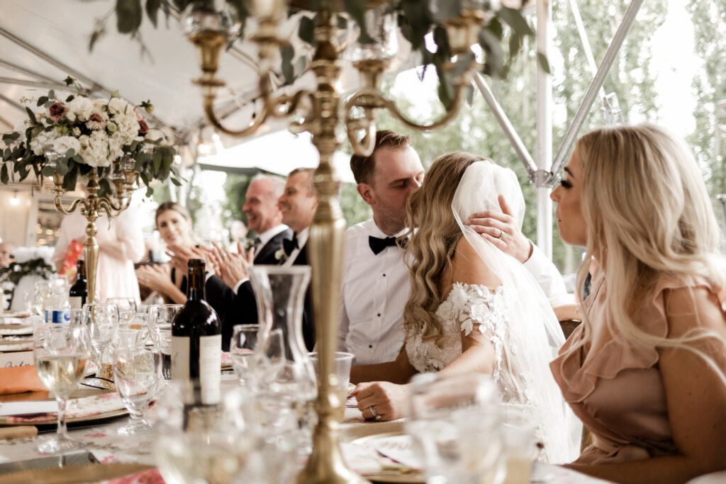 bride and groom share a kiss at the head table at this lakeside wedding at Alberta Beach