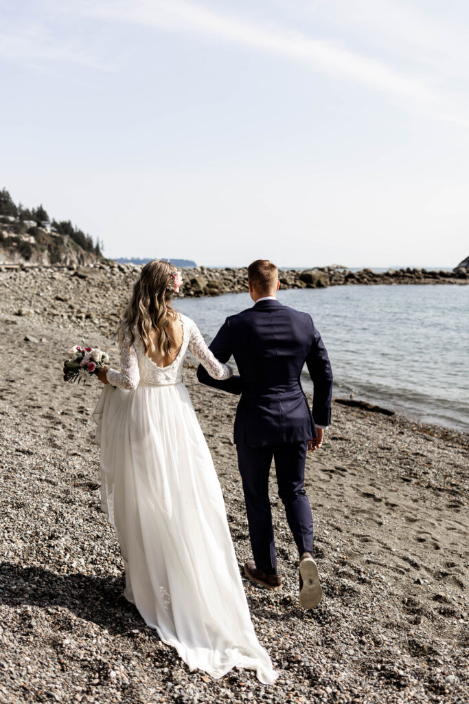 Bride and groom hold hands as they walk down the beach at this Whytecliff Park elopement