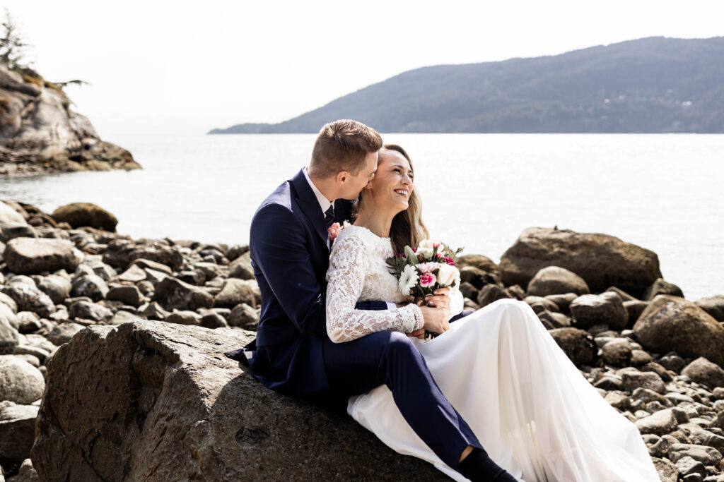 Bride and groom sit together on a rock at this Whytecliff Park elopement