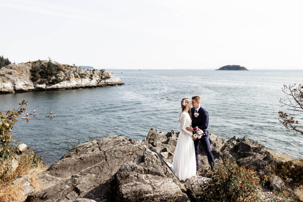 Bride and groom touch noses together in front of a gorgeous blue ocean view at this Whytecliff Park elopement