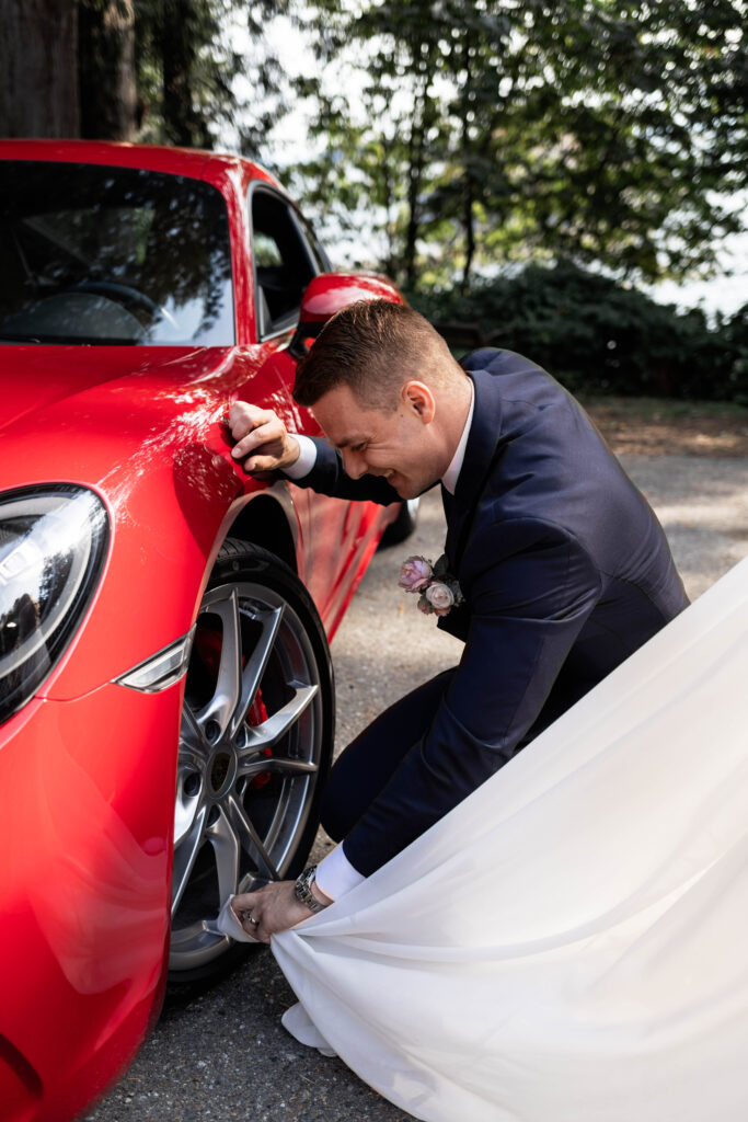 Groom uses the brides dress to shine the tire of a red car at this Whytecliff Park elopement