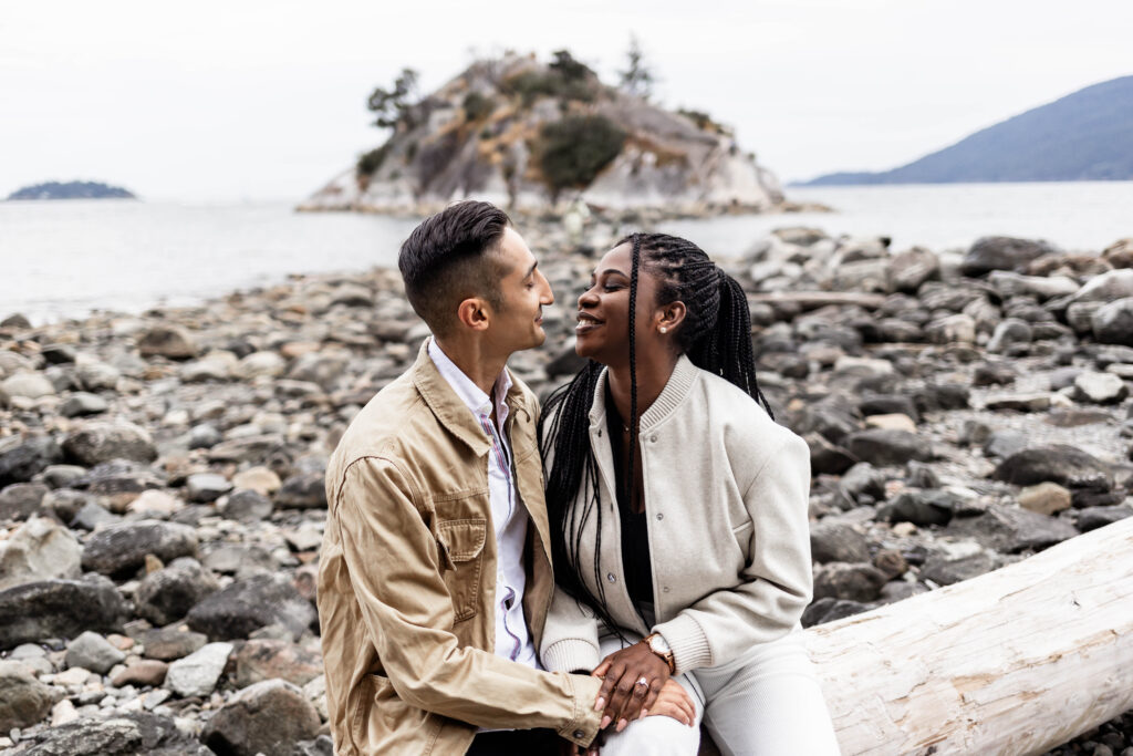 The couple sit on a log on the beach at this Whytecliff Park engagement shoot