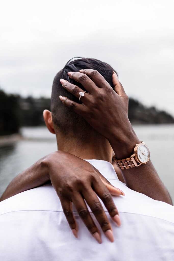 An upclose of Jasmine's hands and engagement ring around Grady's neck at this Whytecliff Park engagement shoot