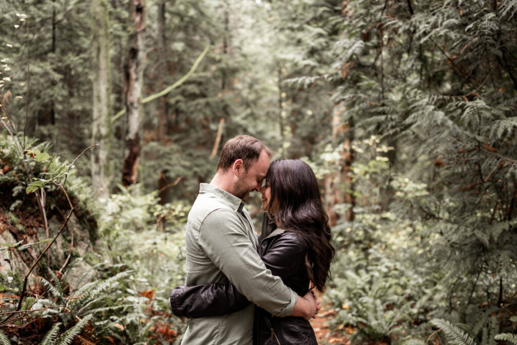 Close-up of a couple embracing with the serene Lighthouse Park landscape in the background.