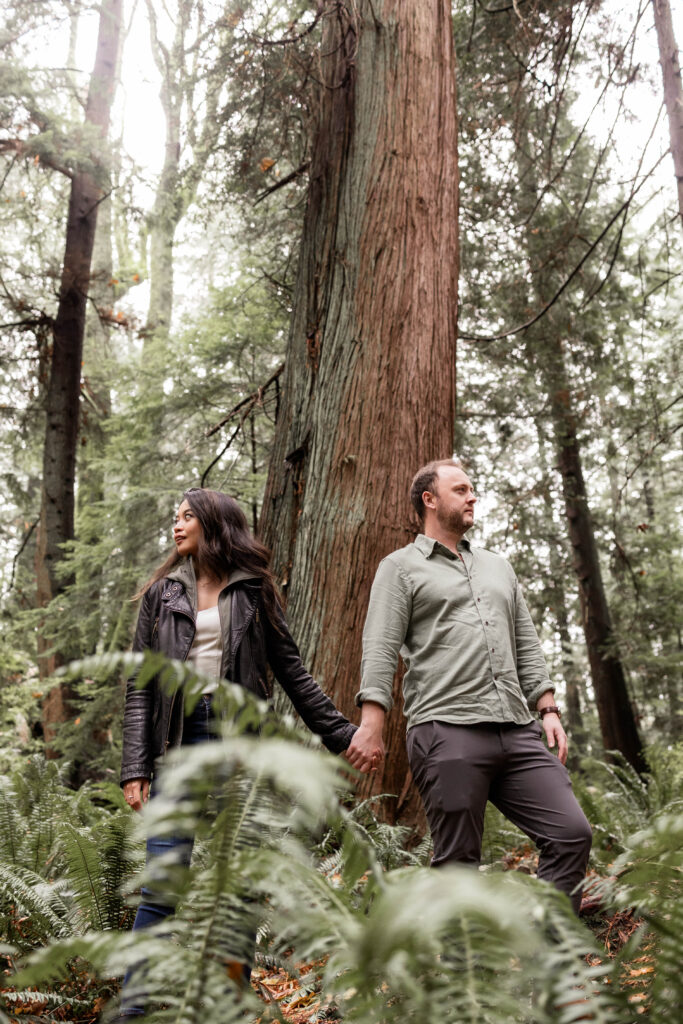 Engaged couple framed by lush greenery during a photoshoot at Lighthouse Park.