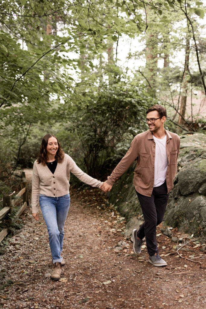 Ben and Stef holding hands walking through the forest at this Lighthouse Park Engagement Shoot