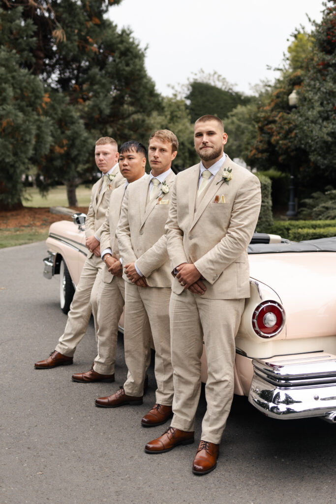 Groomsmen lined up in front of pink vintage car at St Ann's Academy Victoria cathedral wedding