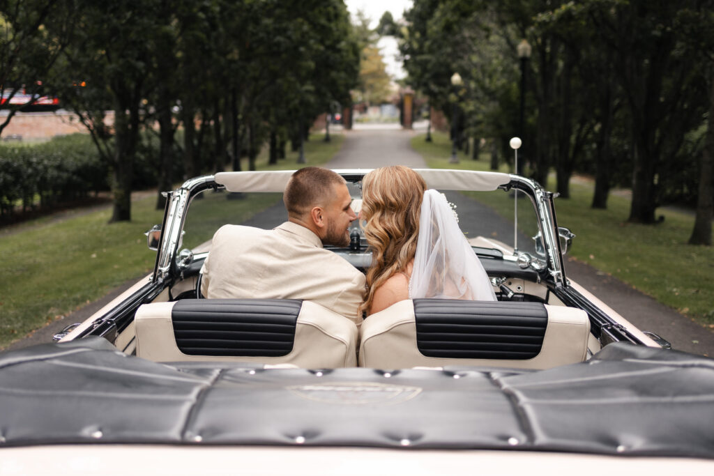 Bride and groom pose for wedding day couples portraits in vintage car at their Victoria cathedral wedding